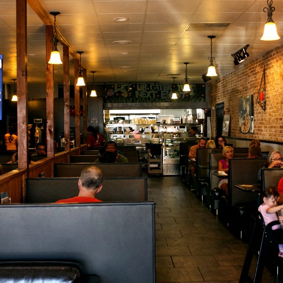 Bustling restaurant interior with diners in booths, a "Please Seat Yourself" sign, and an open kitchen.
