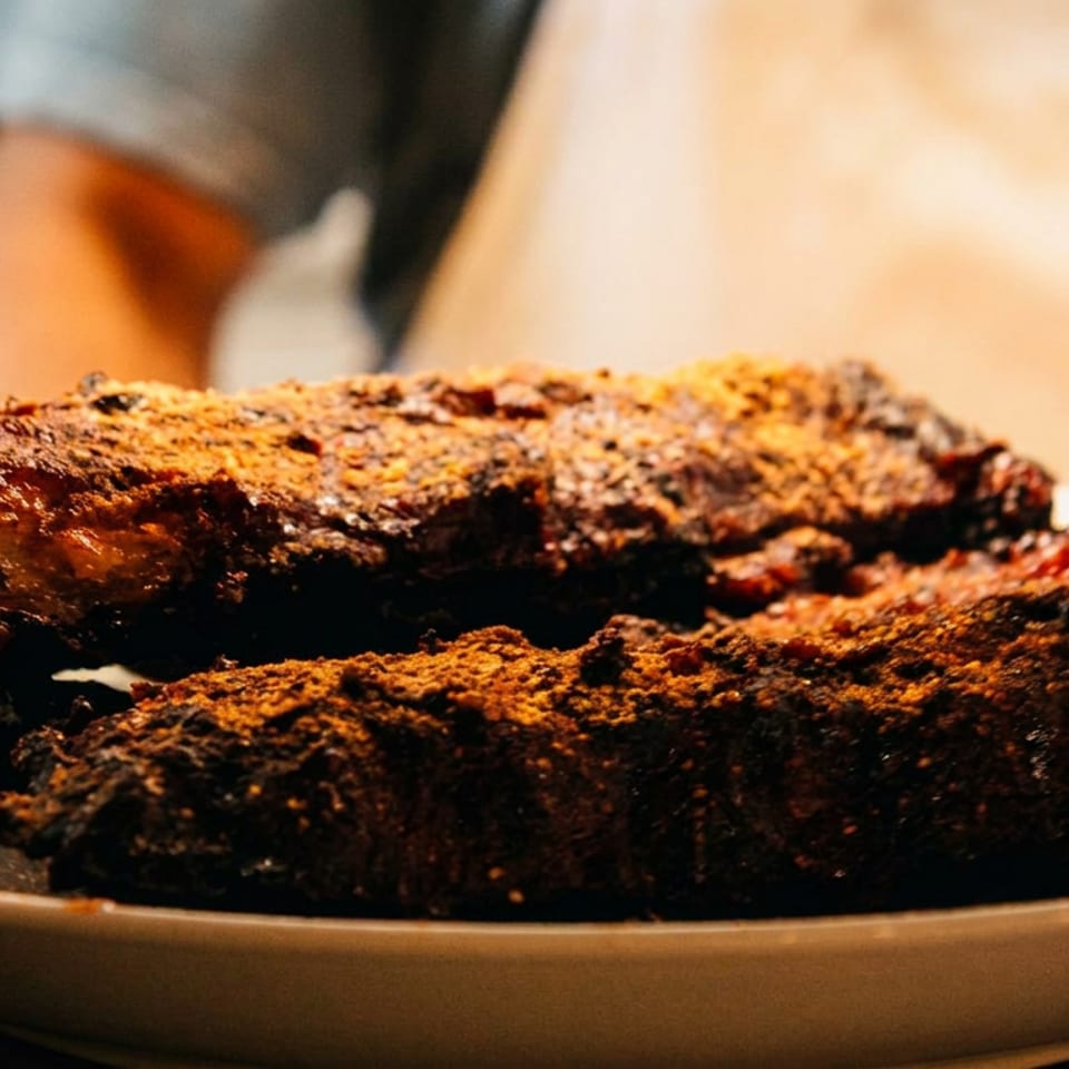 Two pieces of heavily seasoned, barbecued ribs on a white plate.