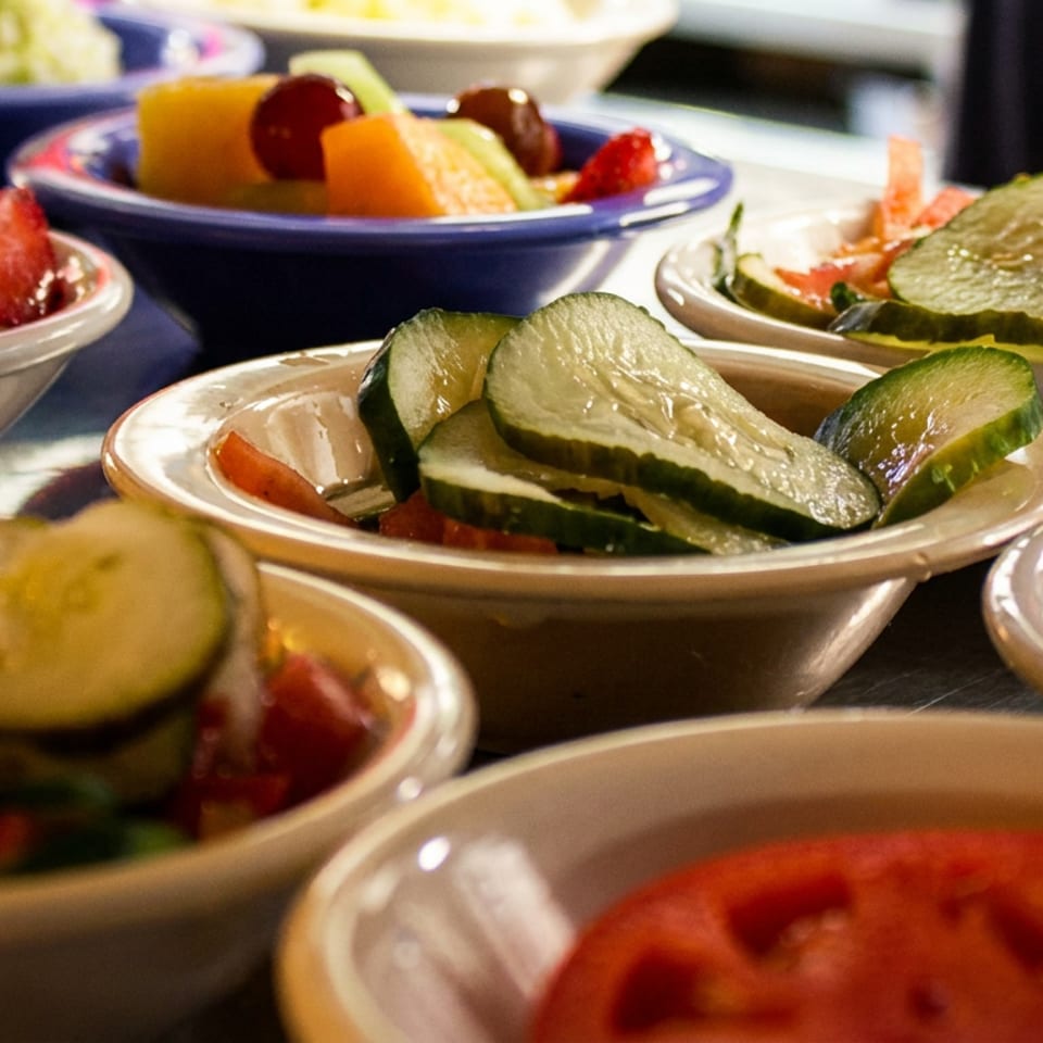 Assorted side dishes including fruit salad, pickles, and sliced tomatoes in small bowls.