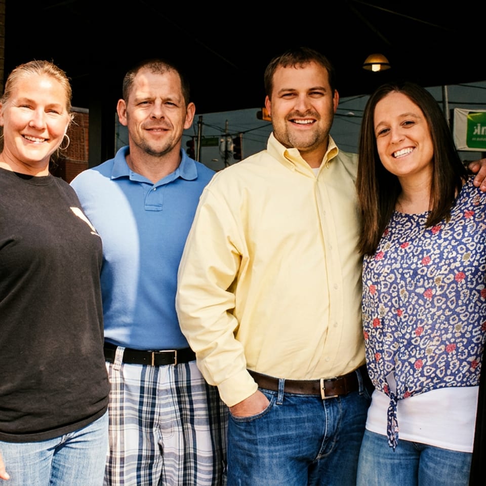 Six smiling restaurant staff members, three men and three women, standing outdoors.